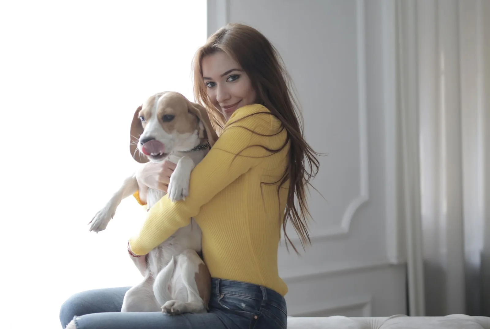 A smiling woman hugging her beagle in a bright living room